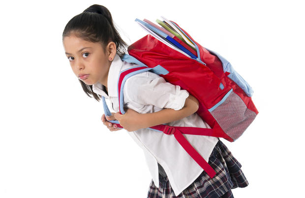 sweet little girl carrying heavy backpack or school bag full  causing stress and pain on back due to overweight isolated on white background