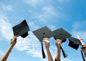 Many hand holding graduation hats on background of blue sky.