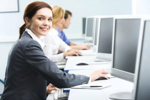 Portrait of busy woman sitting at the computer table and touching computer mouse on the background of businesspeople